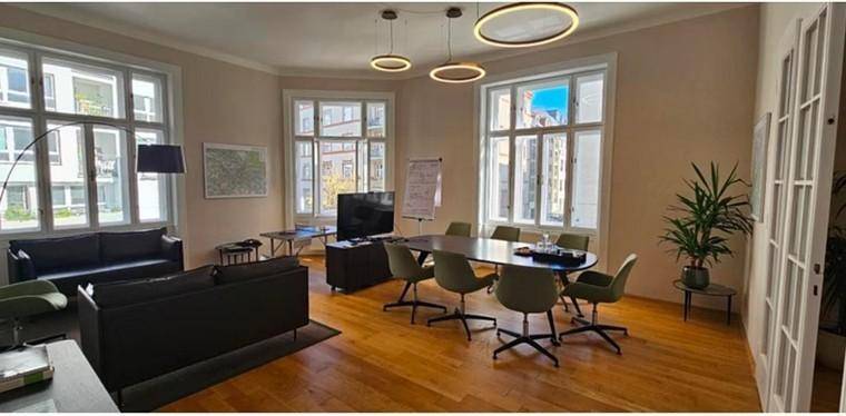 Geräumiger Konferenzraum mit großem Tisch, bequemen Sofas und viel Tageslicht durch hohe Fenster.