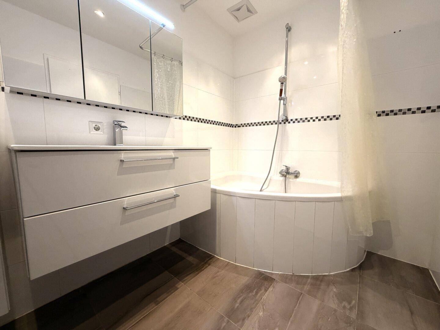 Modernes Badezimmer mit Eckbadewanne, schwebendem Waschtisch und Spiegelschrank.