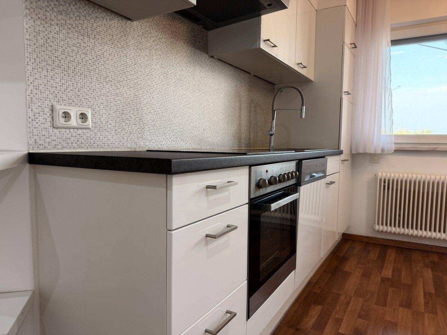 Detailansicht der modernen Küche mit weißen Schränken, dunkler Arbeitsplatte und Mosaik-Fliesenspiegel.