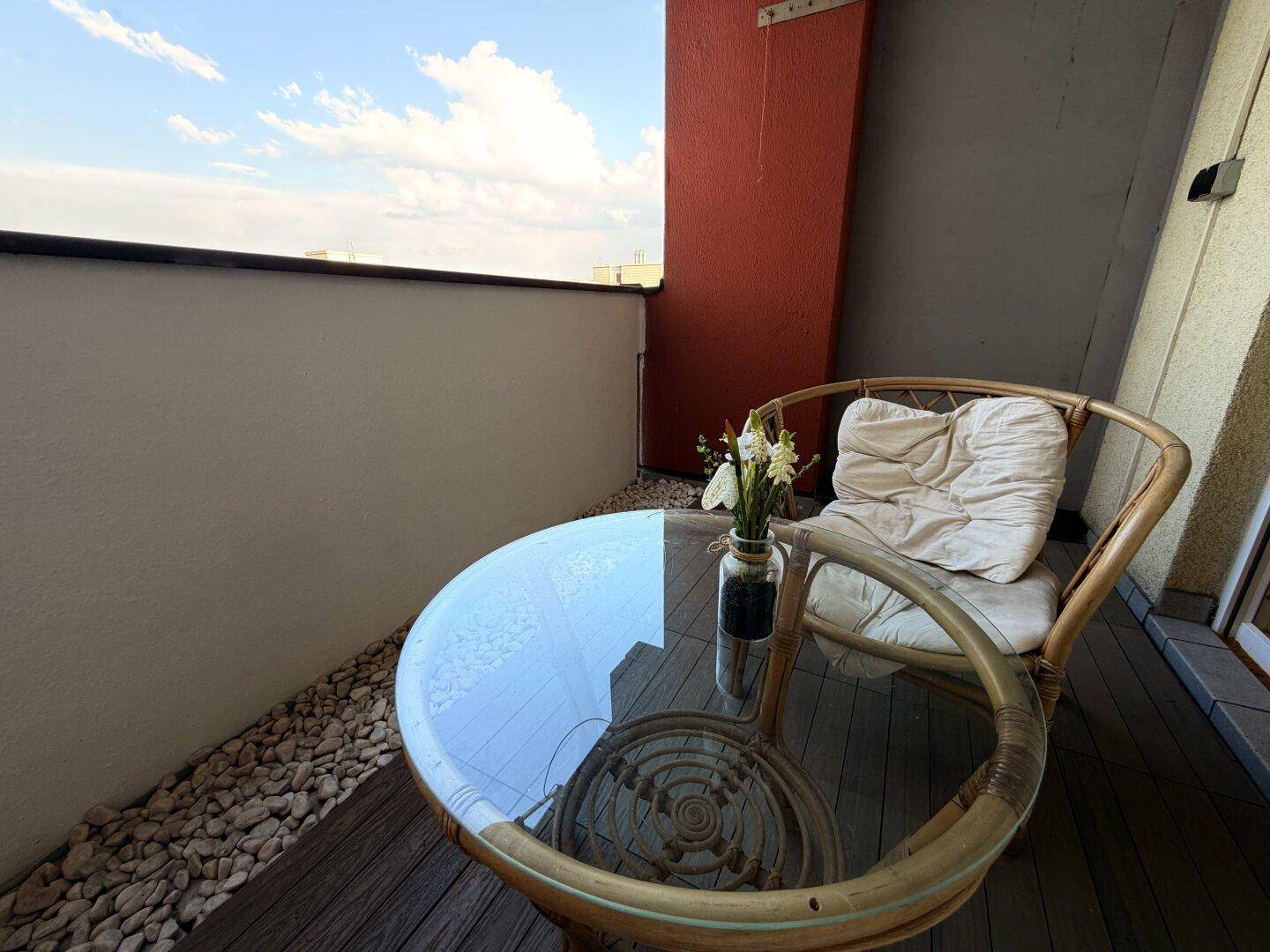 Nahaufnahme des Glastisches und eines Rattanstuhls auf dem Balkon mit Kiesdekor.