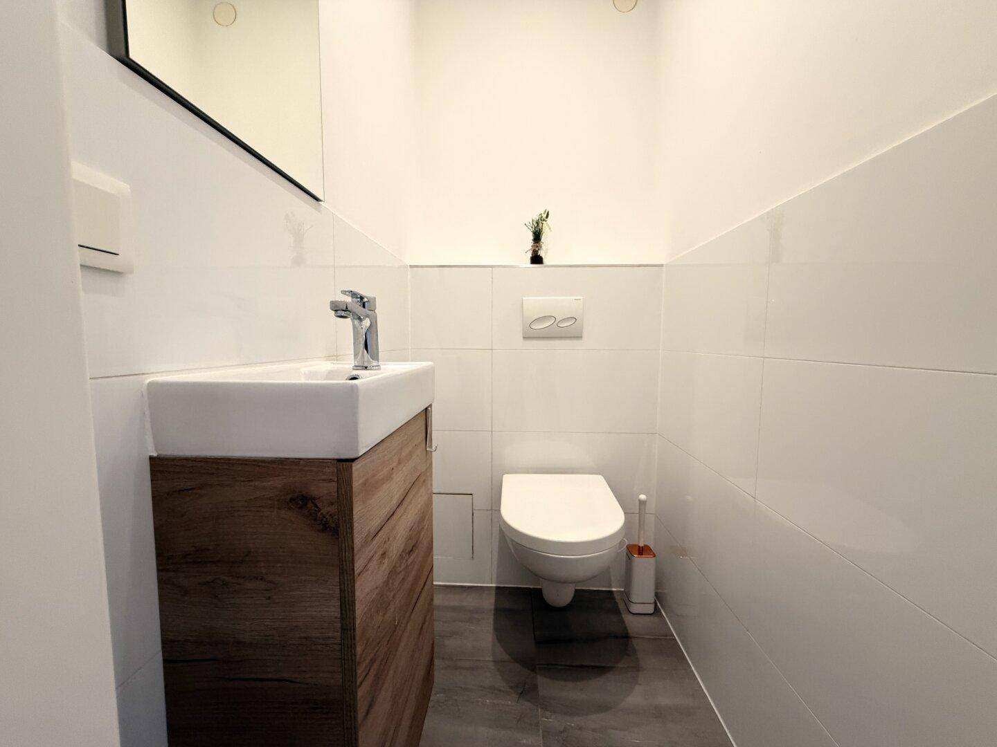 Gäste-WC mit wandhängender Toilette und kleinem Waschtisch mit Holzunterschrank.