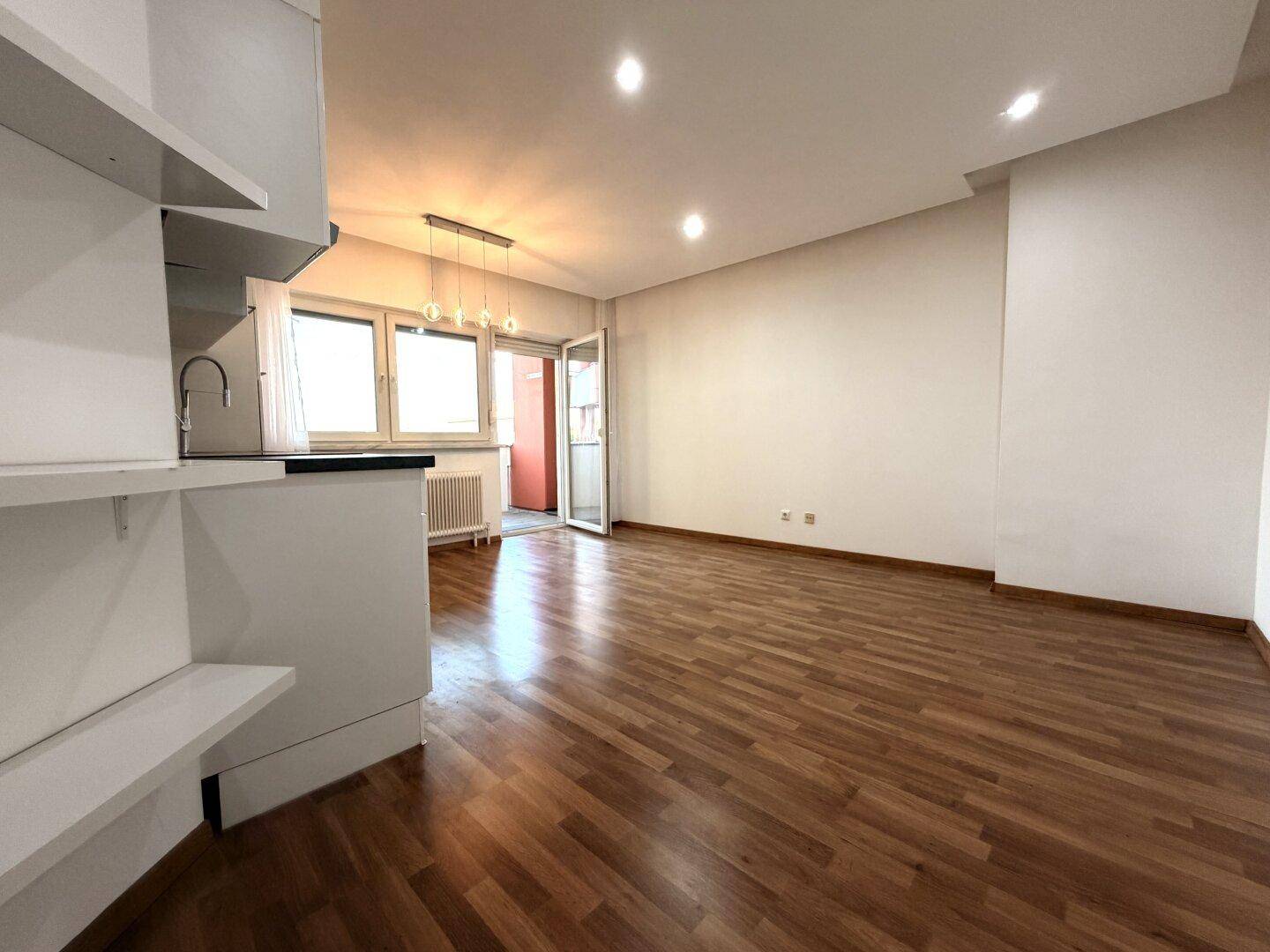 Heller, leerer Wohn-Essbereich mit Holzoptikboden und Zugang zu einem Balkon.