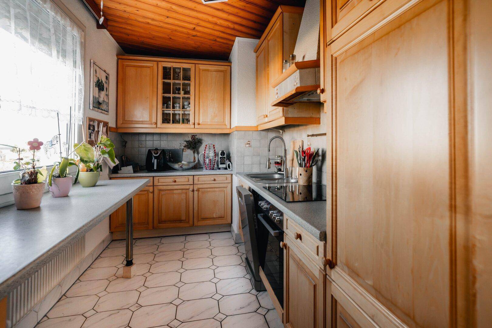 Funktionale Küche mit Holzschränken, Fliesenboden und Fenster, gut ausgestattet für den täglichen Gebrauch.