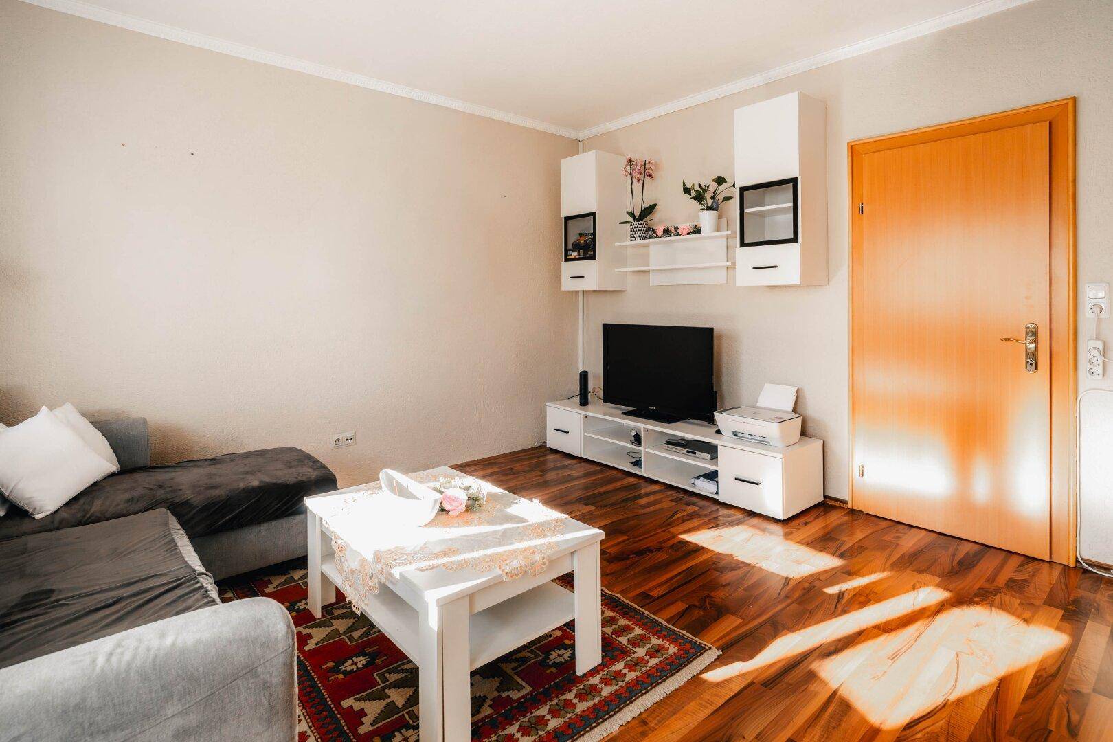 Helles Wohnzimmer mit Sofa, Fernseher und Holzboden, ideal für entspannte Abende und Unterhaltung.