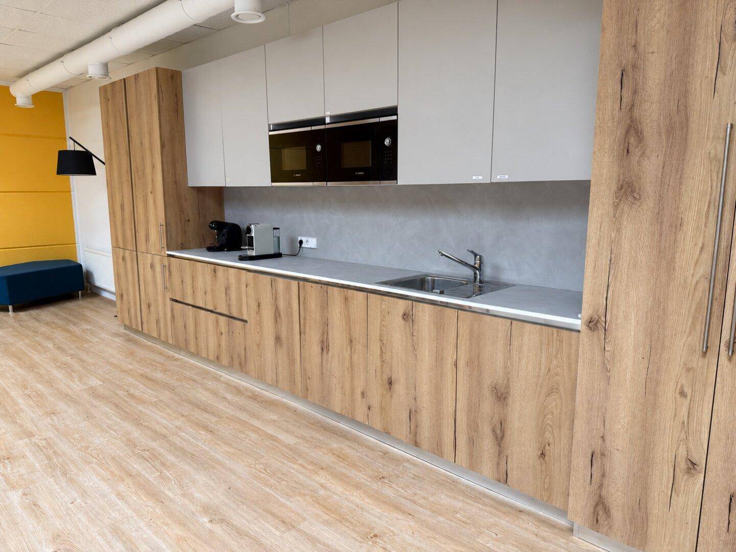 Helle Büroküche mit Holzfronten, weißen Oberschränken und modernen Einbaugeräten, ideal für Mitarbeiter.