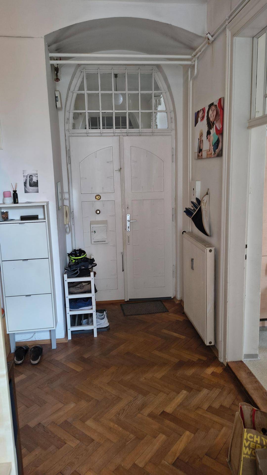 Eingangsbereich mit Fischgrätparkett, Schuhregal und einer großen Doppeltür im Altbaustil.