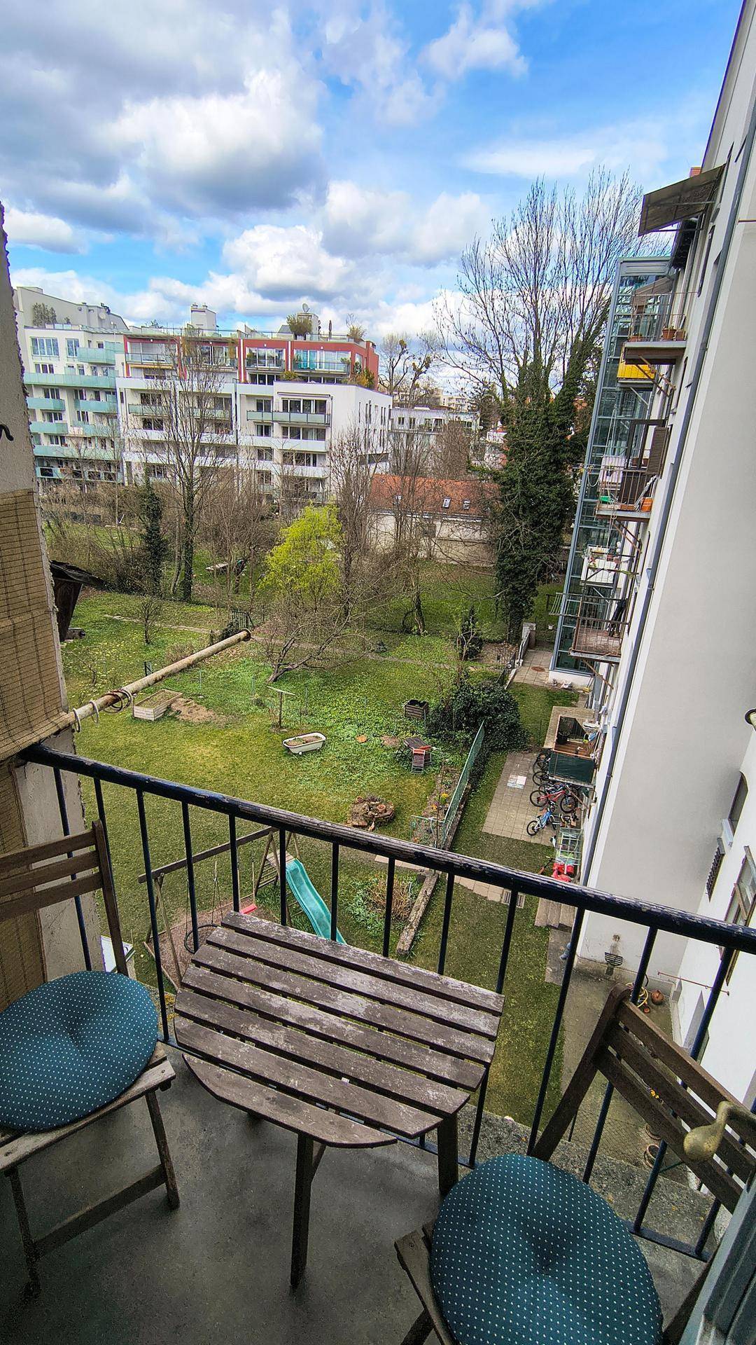 Balkon mit Holztisch und Stühlen, bietet einen grünen Blick auf den ruhigen Hinterhof.