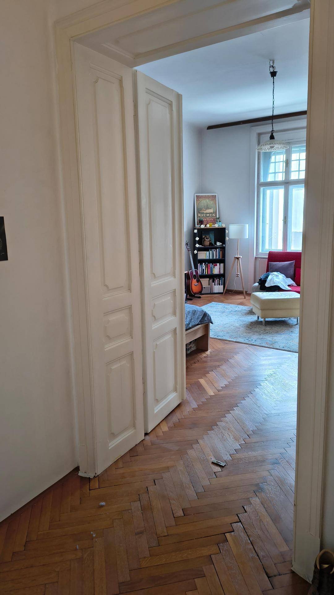 Blick vom Flur in ein helles Zimmer mit Fischgrätparkett und einem roten Sofa, typisch für Altbauten.