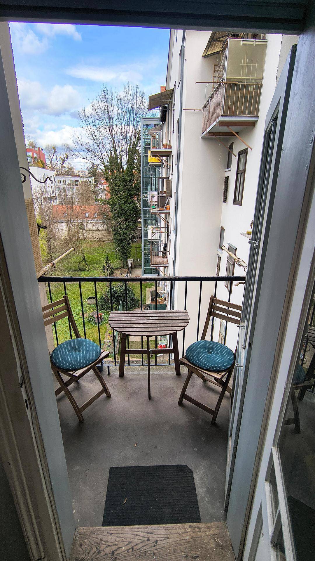 Balkon mit Holztisch und Stühlen, mit Blick auf den grünen Innenhof und die umliegenden Gebäude.
