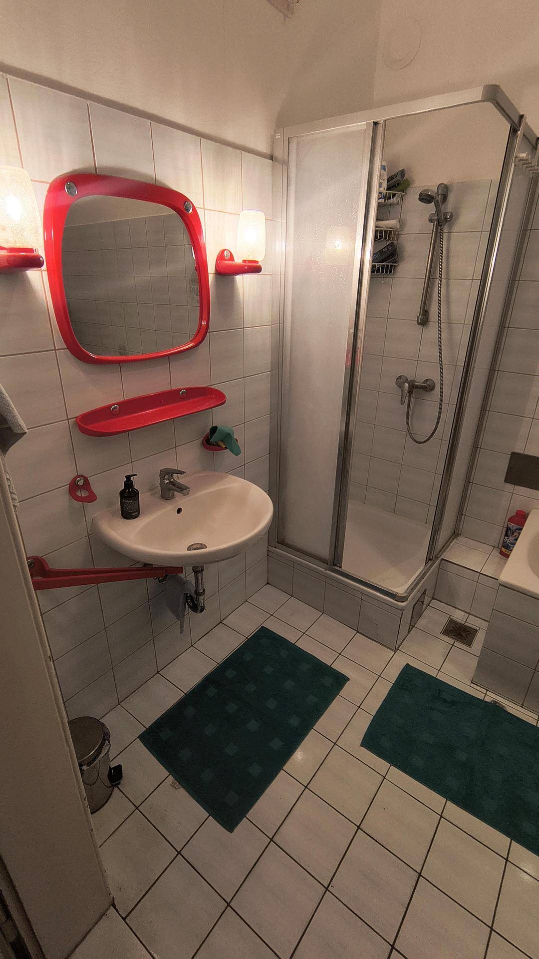 Badezimmer mit Dusche, Waschbecken und einem roten Spiegel, im Stil der 80er Jahre.