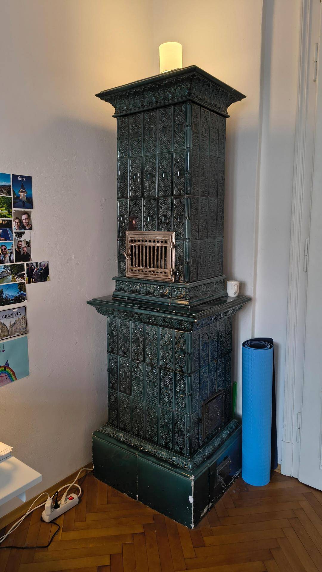 Detailansicht eines traditionellen grünen Kachelofens als Heizelement in einem Altbauzimmer.