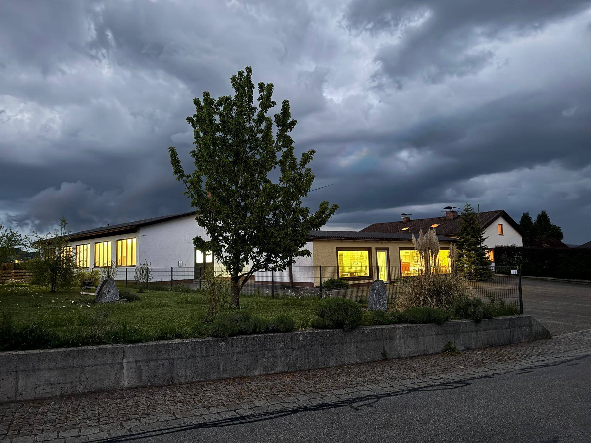 Gebäudeansicht bei Dämmerung mit beleuchteten Fenstern und dunklem Himmel über dem Vorplatz.