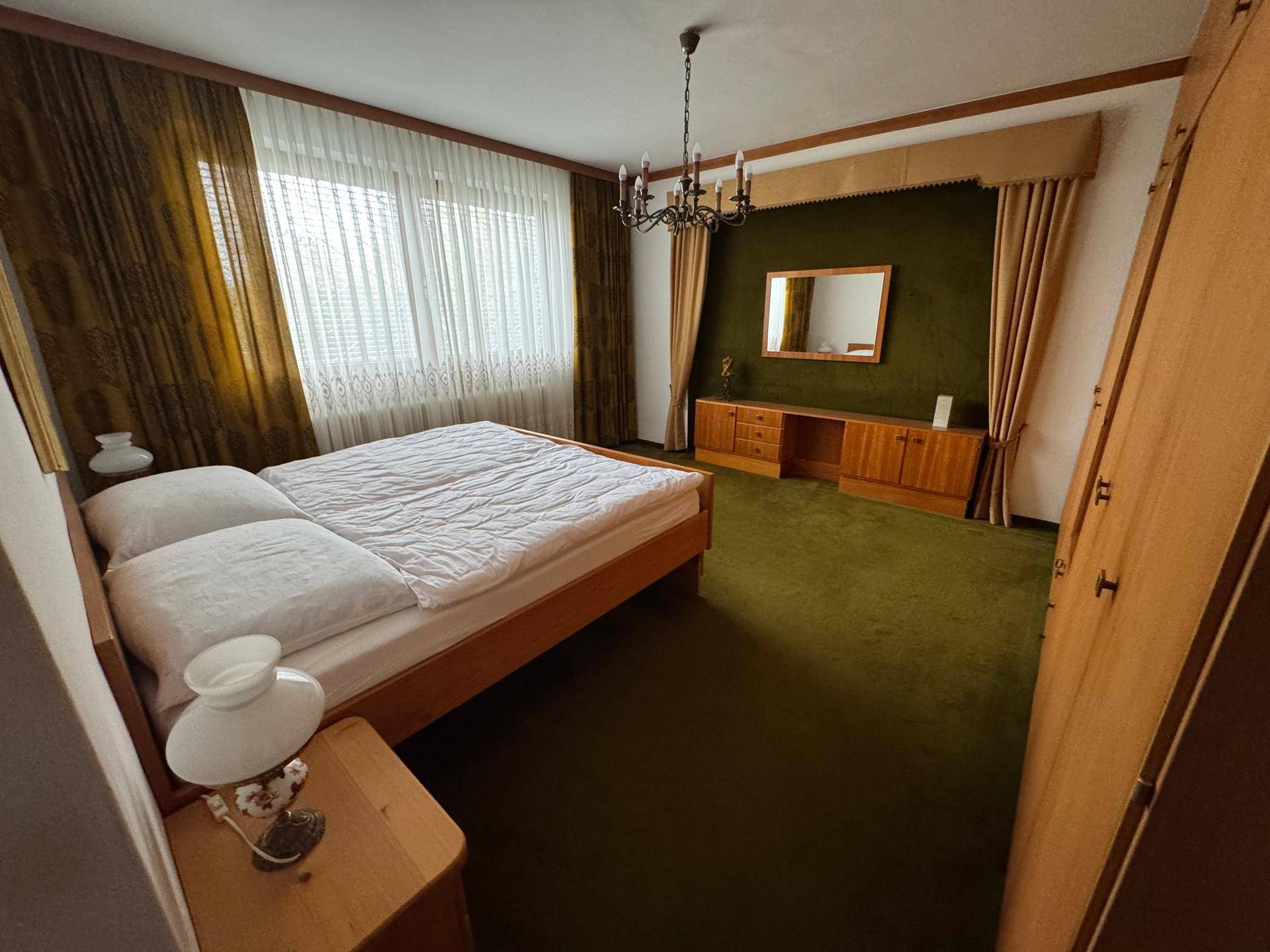 Schlafzimmer mit grünem Teppichboden, Holzmöbeln und großen Fenstern.