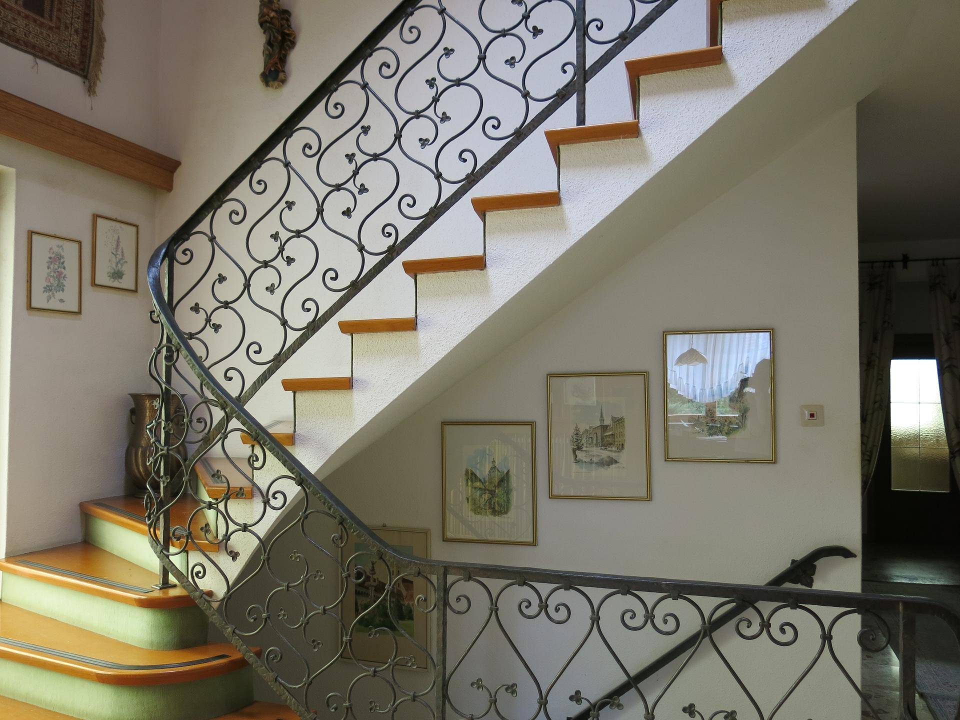 Elegante Treppe mit schmiedeeisernem Geländer und Holzstufen in einem hellen Flur.