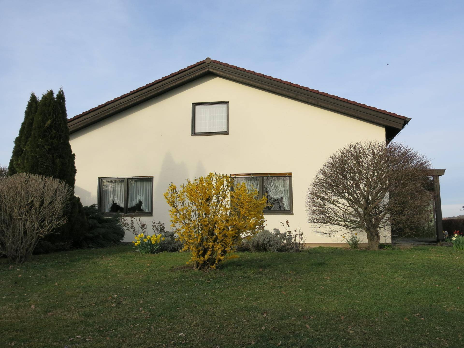 Seitenansicht des Wohnhauses mit Gartenbereich und blühenden Sträuchern im Frühling.