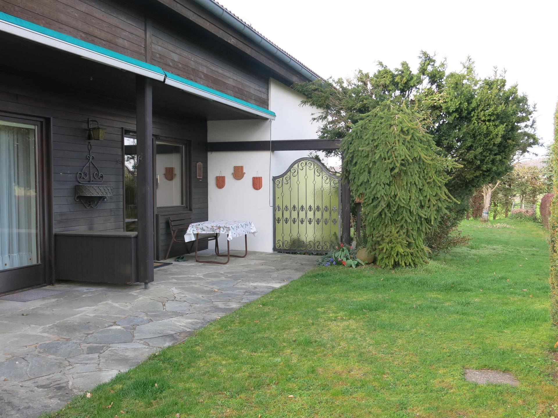 Gepflasterte Terrasse neben dem Haus mit Zugang zum Garten und schmiedeeisernem Tor.