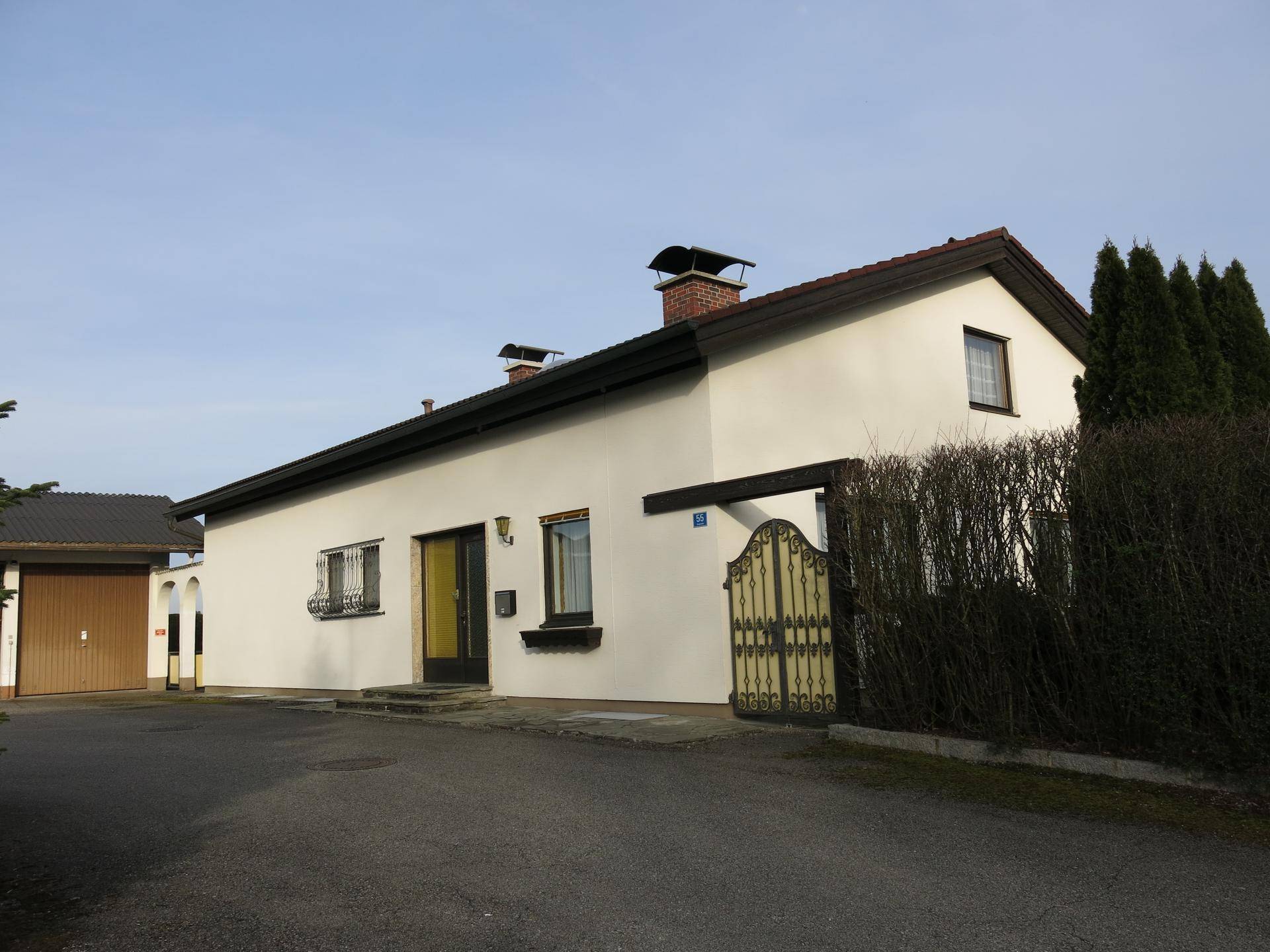 Eingangsbereich des Wohnhauses mit gelbem Tor und gepflegter Hecke unter blauem Himmel.