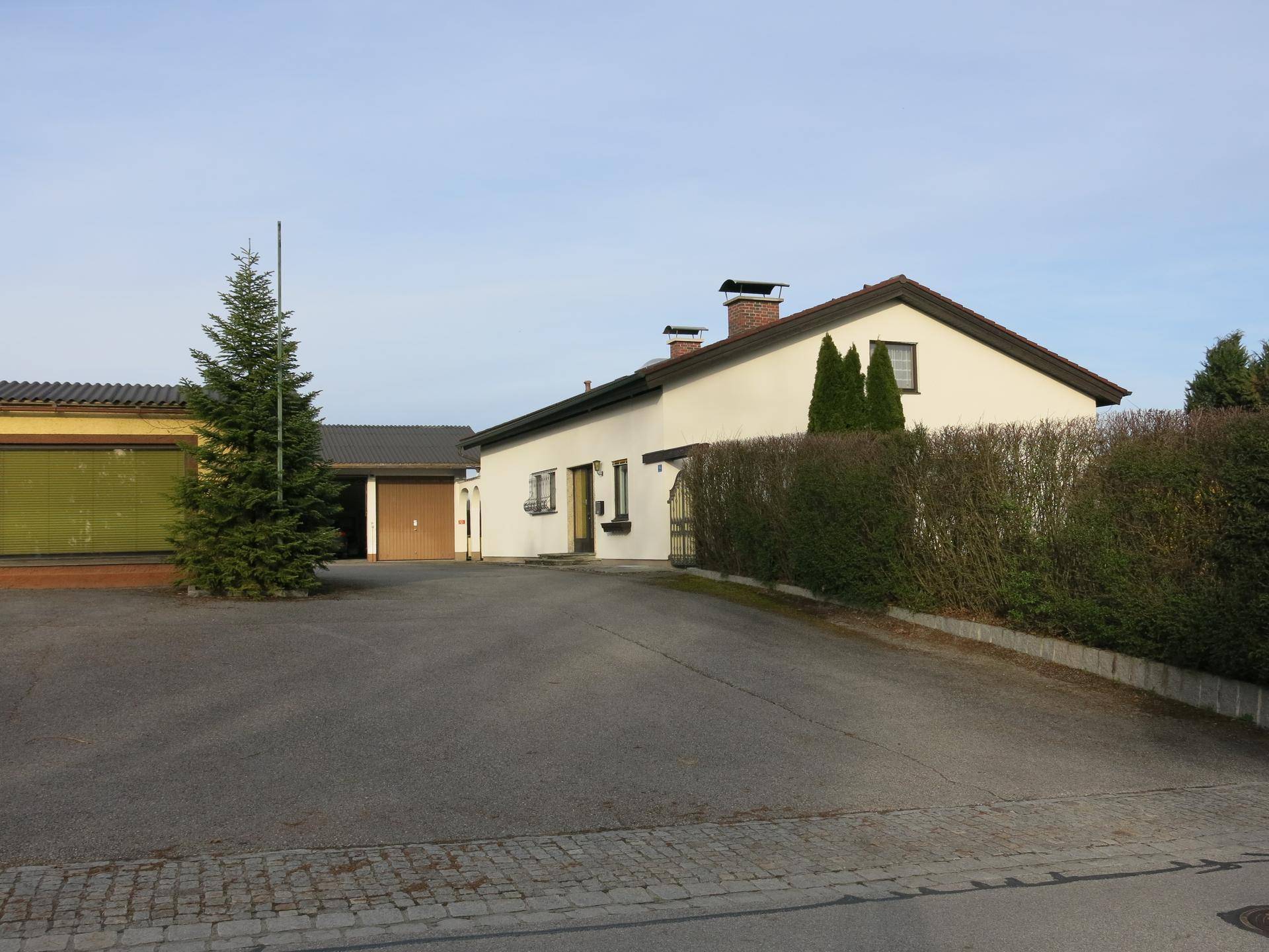 Wohnhaus mit Satteldach und angrenzender Garage, umgeben von Hecken und Bäumen.