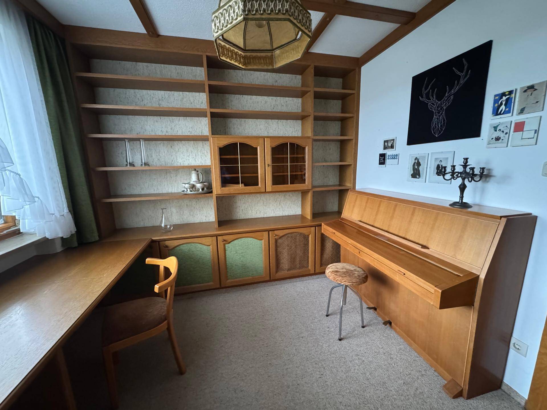 Arbeitszimmer mit großer Bücherwand, Klavier und Teppichboden unter Holzdecke.