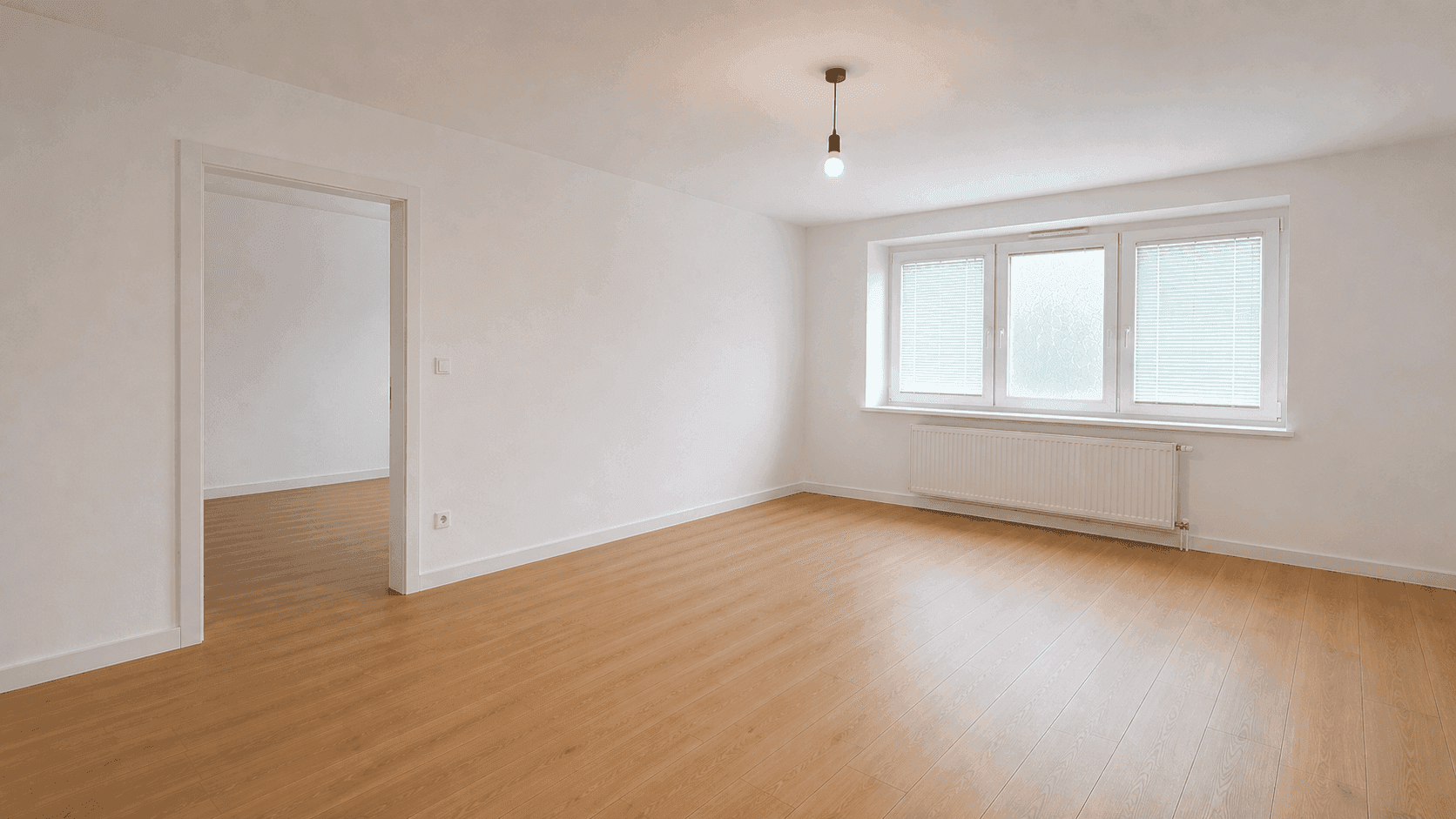 Heller Wohnraum mit Holzfußboden, weißen Wänden und großem Fenster.