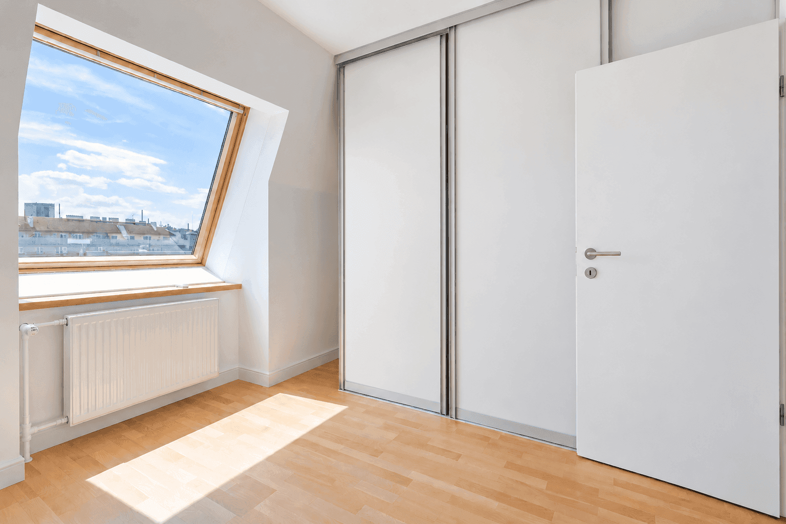 Schlafzimmer mit Holzfußboden, Dachschrägenfenster und integrierten Schiebetürenschränken.