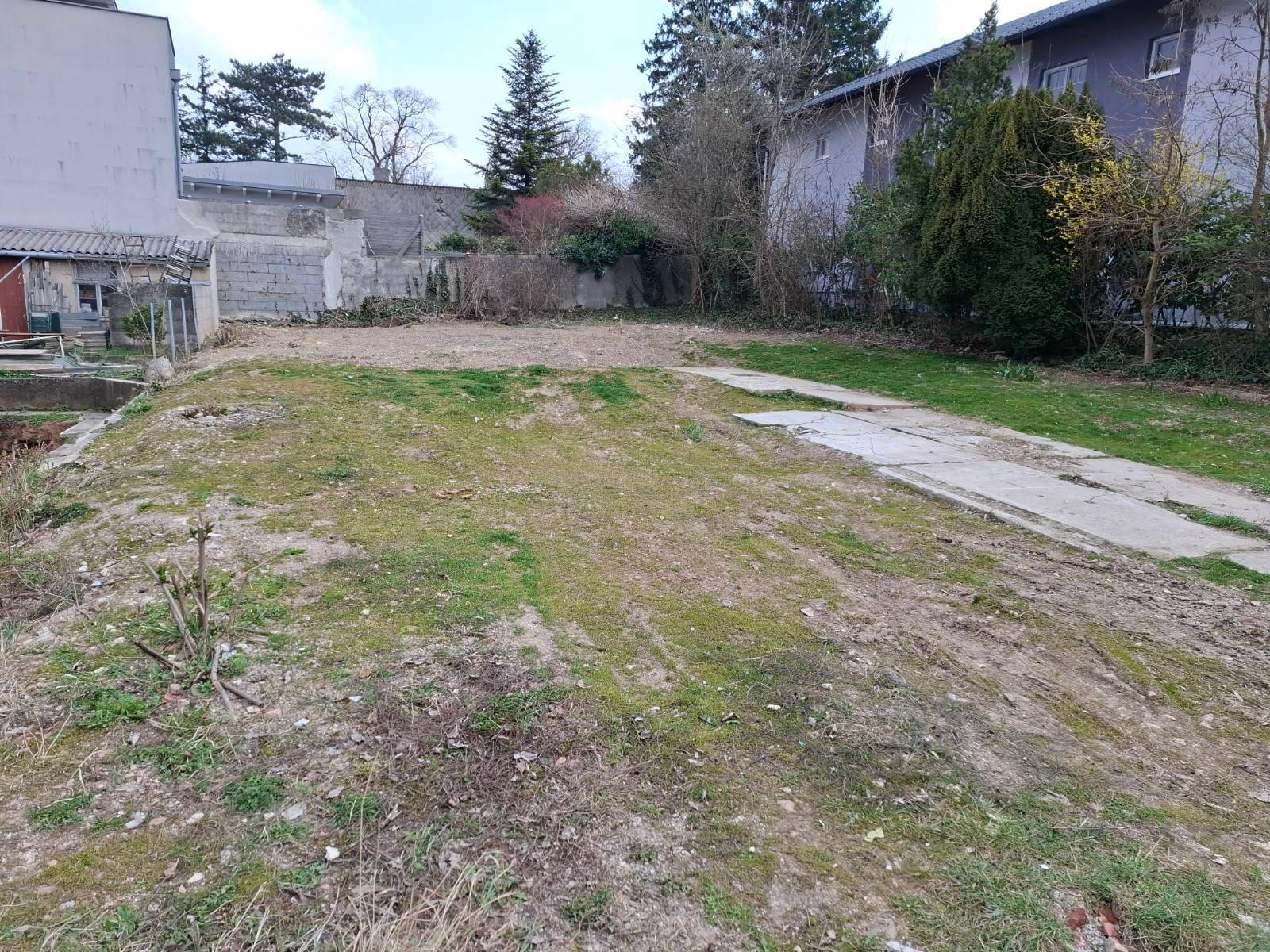 Weitläufiges, ungenutztes Grundstück mit spärlicher Vegetation und angrenzenden Gebäuden.