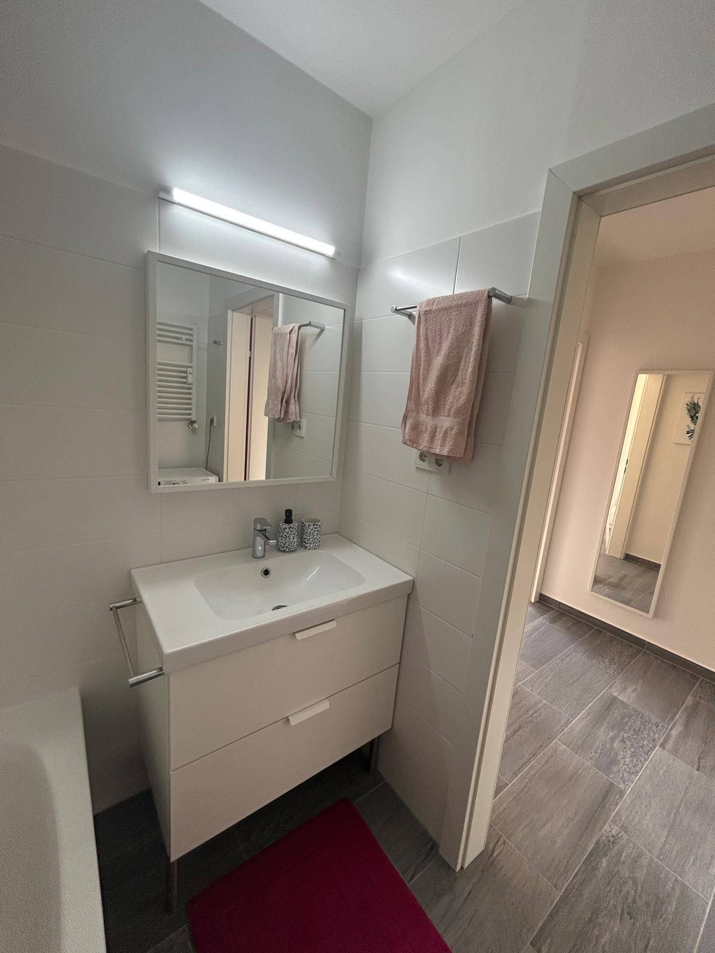 Modernes Badezimmer mit Waschtisch, Spiegelschrank und Handtuchhalter.