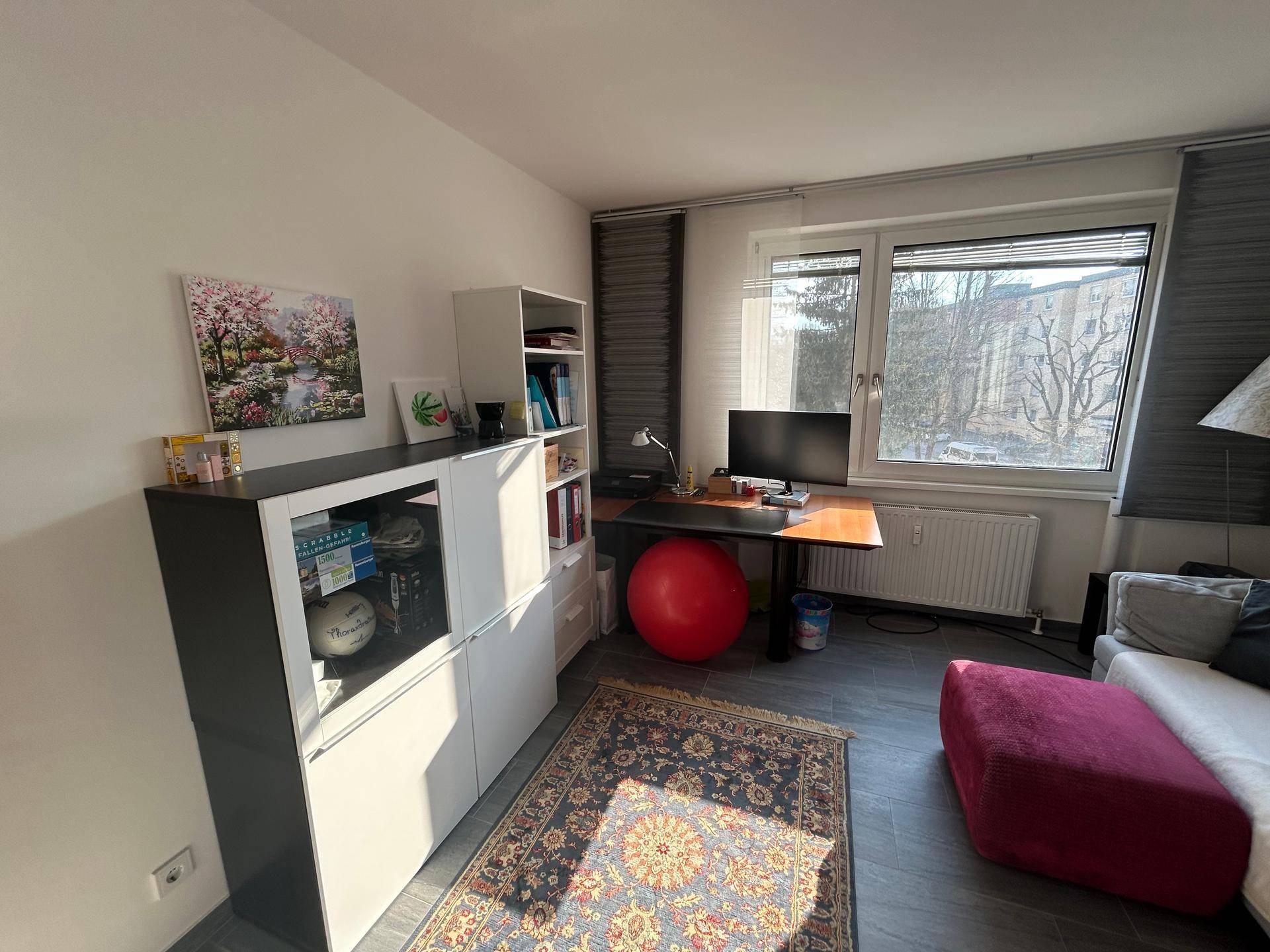 Helles Arbeitszimmer mit Schreibtisch, Regalen und Teppich auf Fliesenboden.