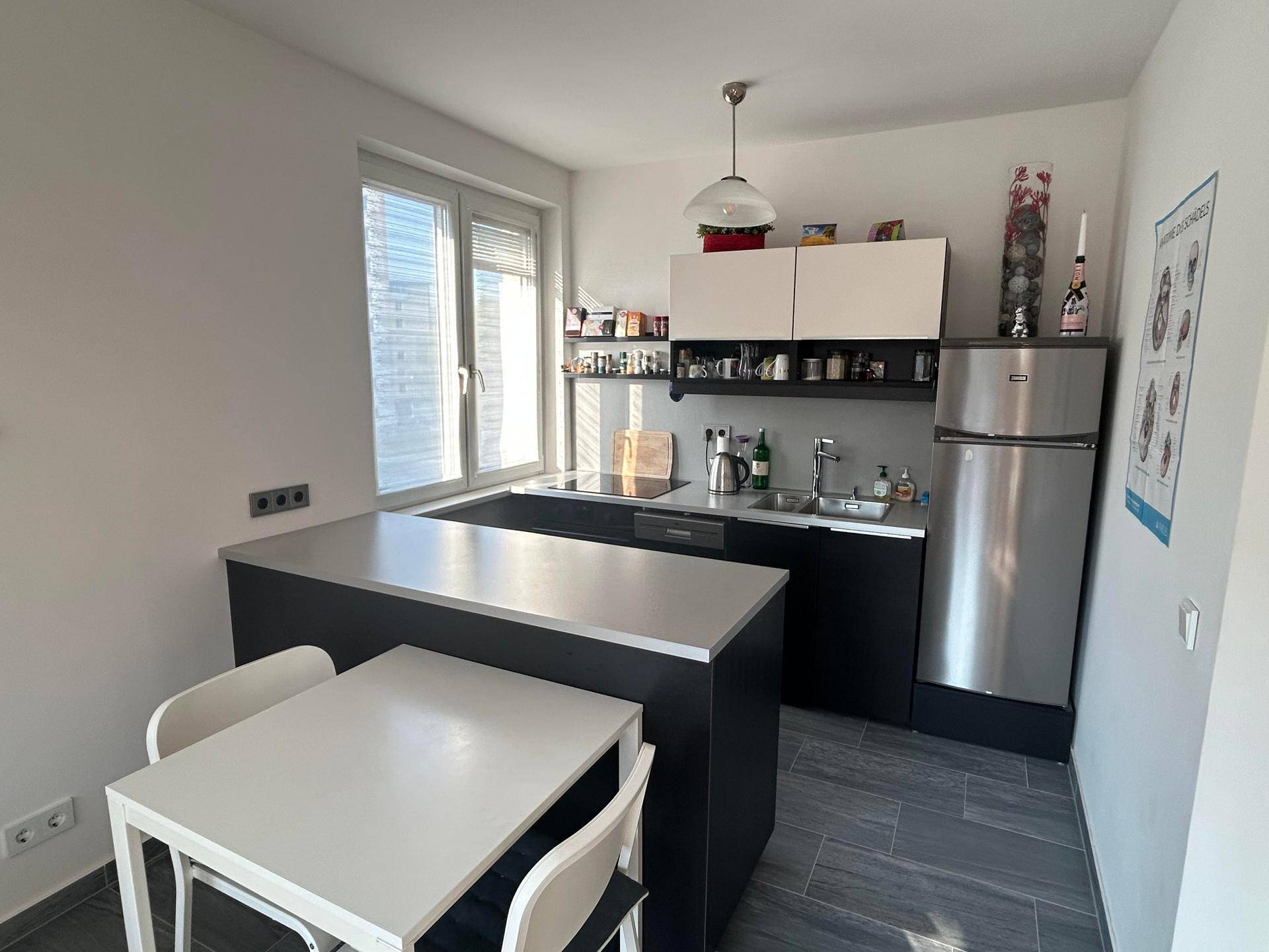 Moderne Küchenzeile mit integriertem Essbereich, Edelstahlkühlschrank und großem Fenster.