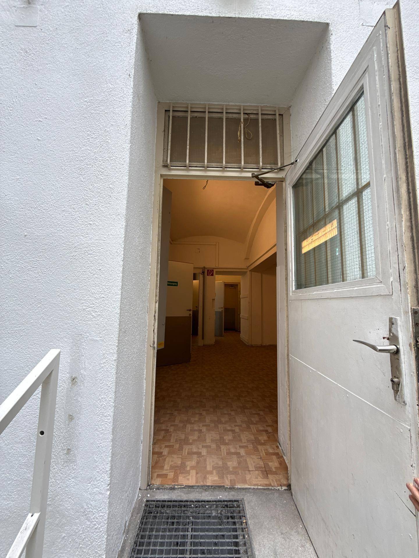Eingangsbereich mit offener Tür, die in einen langen Flur mit Holzboden führt.