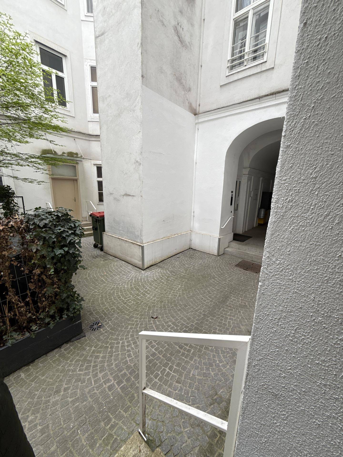 Gepflasterter Innenhof mit Grünflächen und Zugang zu den Gebäudeeingängen, bietet ruhige Atmosphäre.
