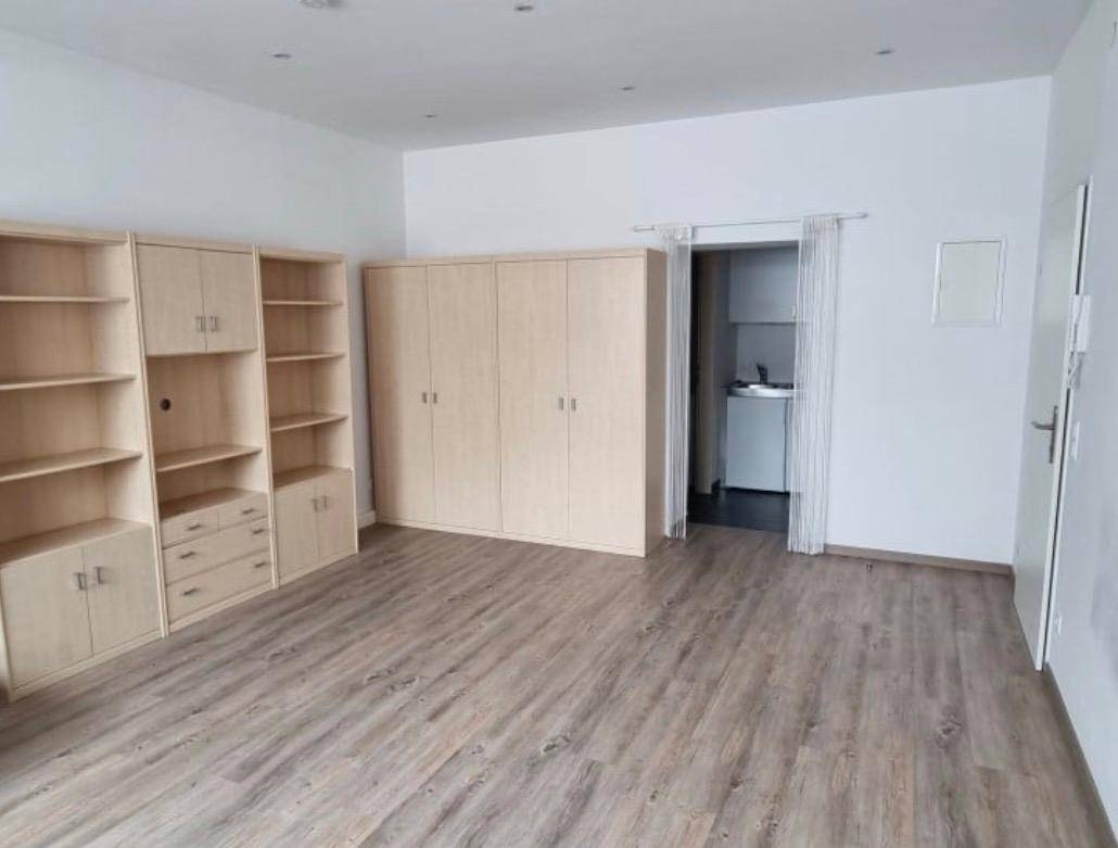 Geräumiger Wohnbereich mit Laminatboden, Holzregalen und Zugang zu einer Kochnische.