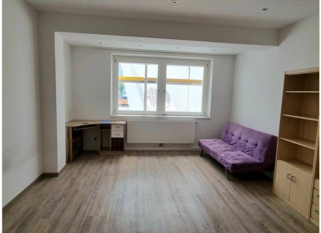 Helles Wohnzimmer mit Laminatboden, großem Fenster und einem lila Sofa.