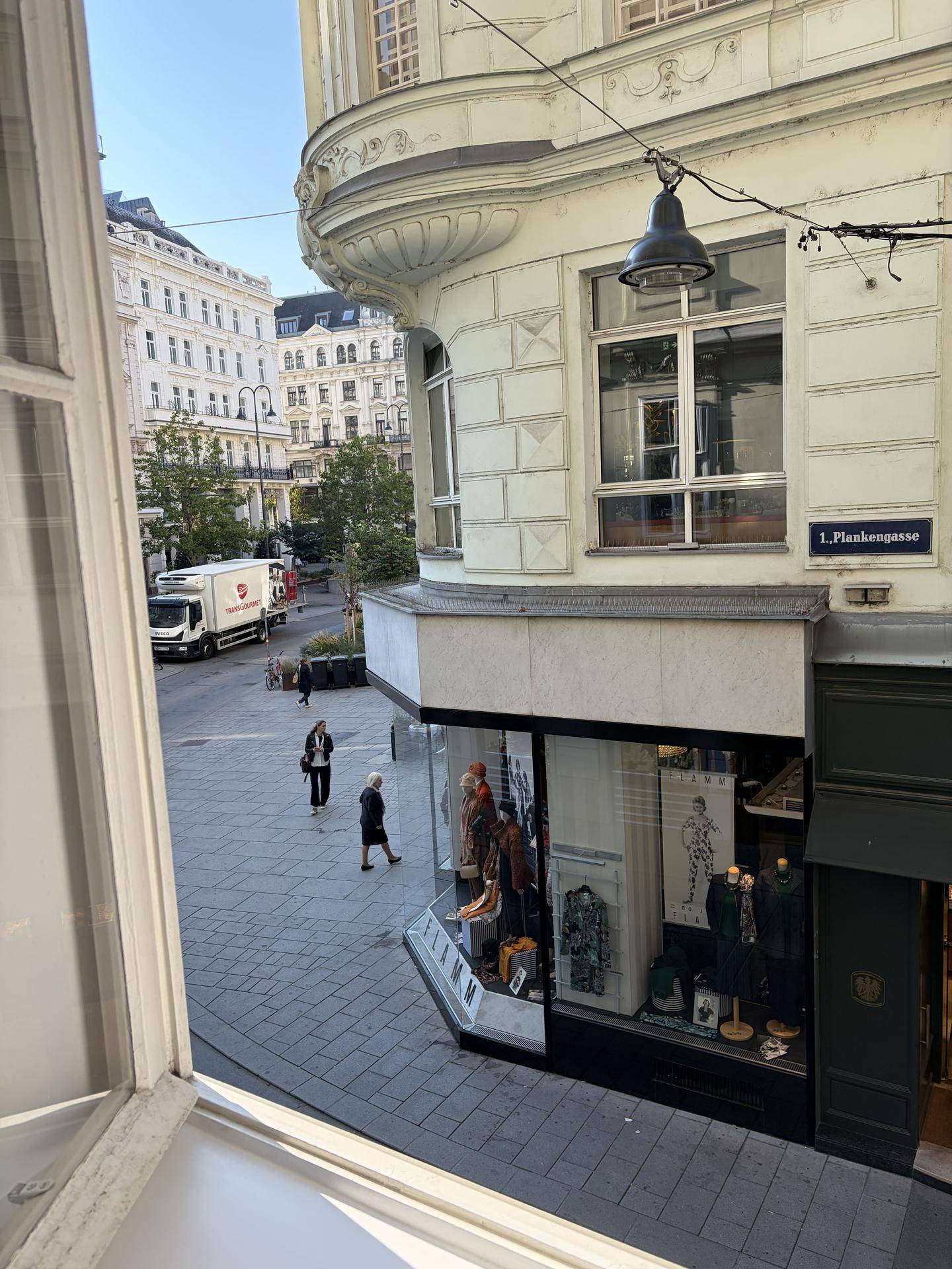 Blick aus dem Fenster auf eine belebte Stadtstraße mit historischen Gebäuden und Passanten.