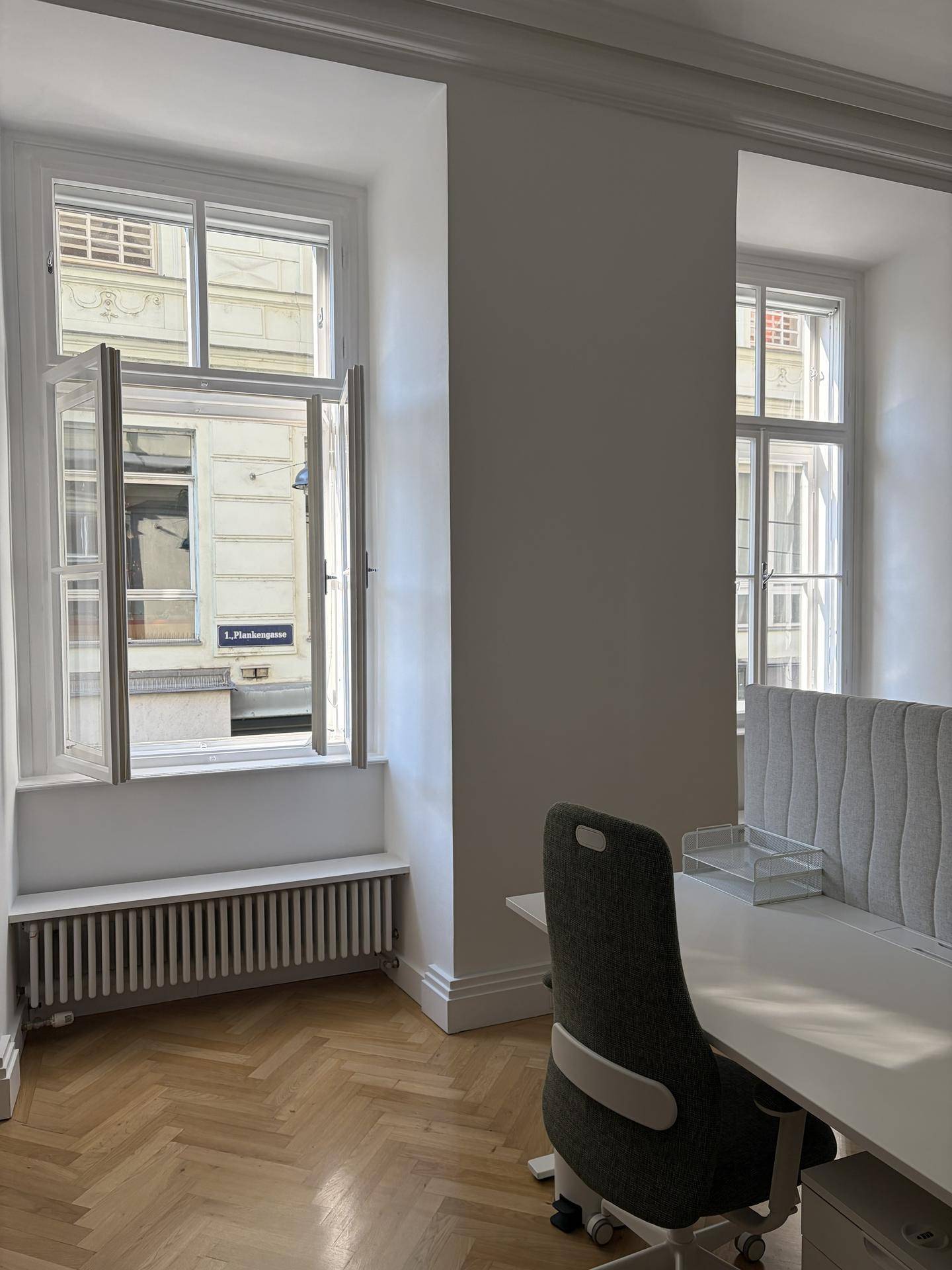 Büro mit geöffnetem Fenster, das einen Blick auf die Straße bietet, ausgestattet mit Schreibtisch und Heizkörper.