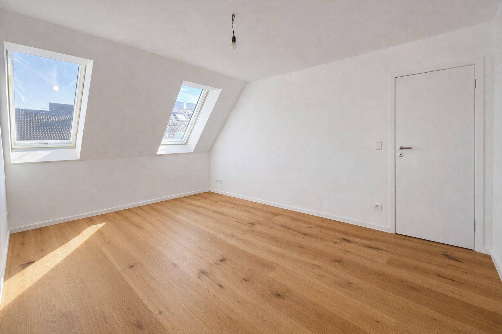 Helles Dachzimmer mit Holzboden, zwei Dachfenstern und einer modernen Tür.