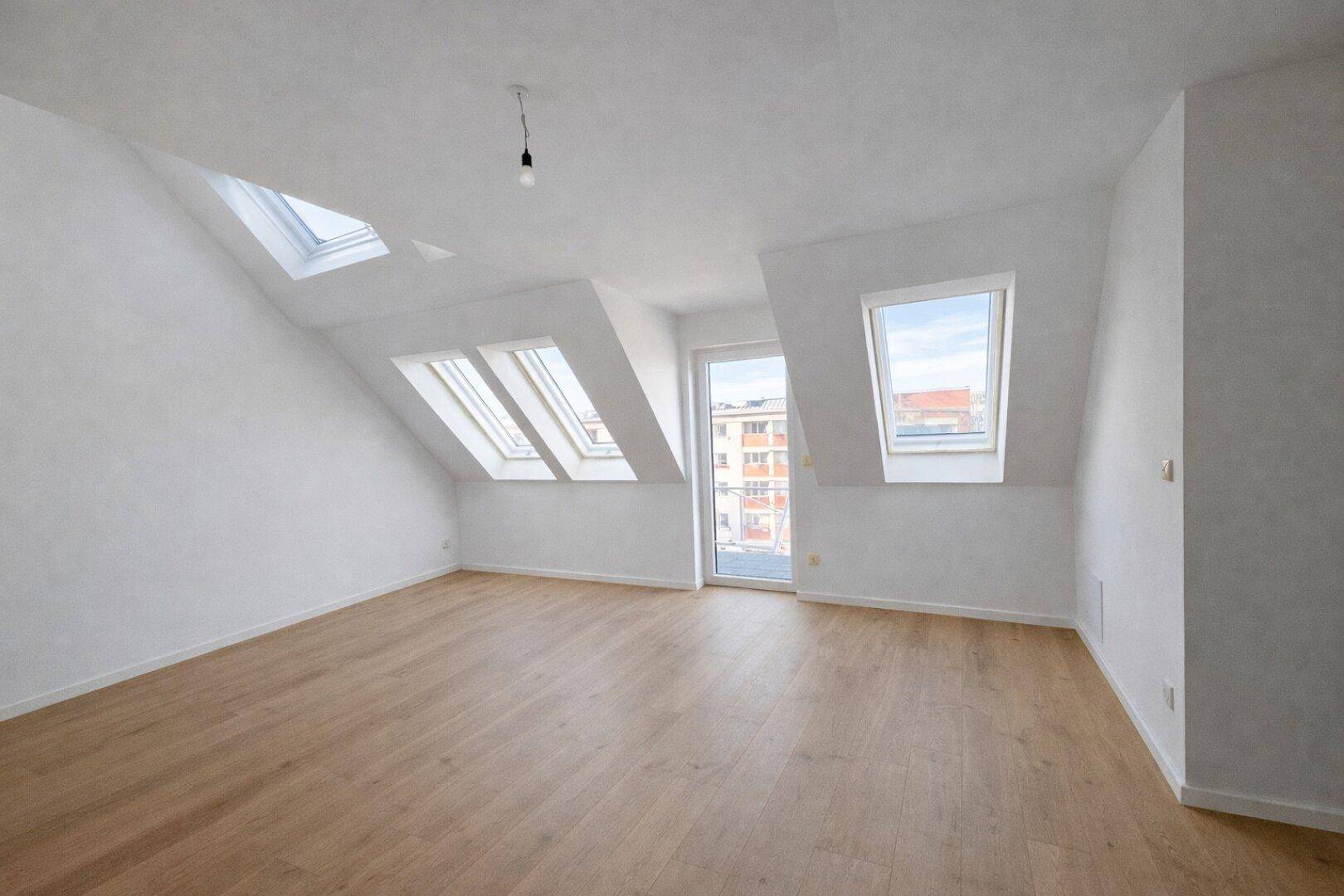 Geräumiges Dachzimmer mit Holzboden, Dachfenstern und Zugang zu einem französischen Balkon.