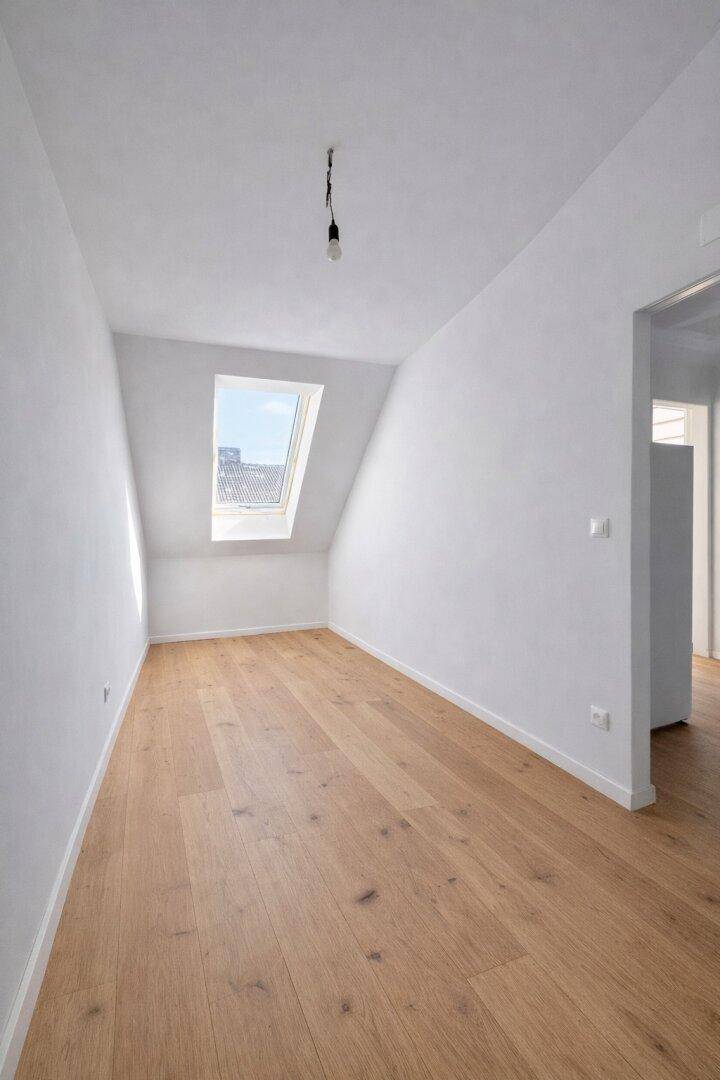 Heller Raum im Dachgeschoss mit einem Dachfenster und hochwertigem Holzparkett.