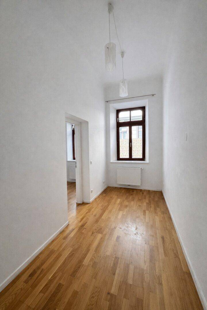 Schmaler Flur mit Holzboden und einem Fenster, der zu weiteren Räumen führt.