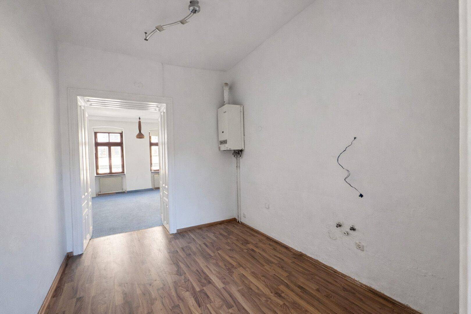Kleiner Raum mit Laminatboden, weiß gestrichenen Wänden und einem an der Wand montierten Warmwasserbereiter.