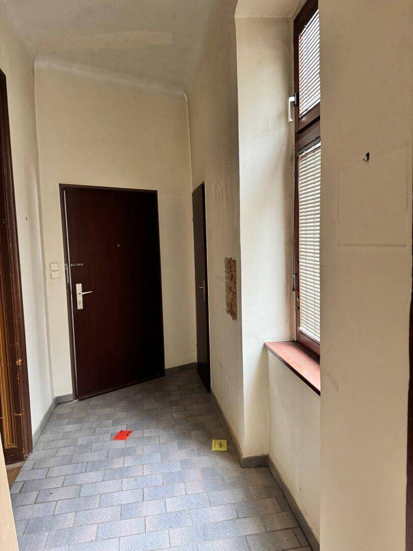 Langer Flur mit Fliesenboden und einem Fenster, das Tageslicht hereinlässt und den Bereich erhellt.
