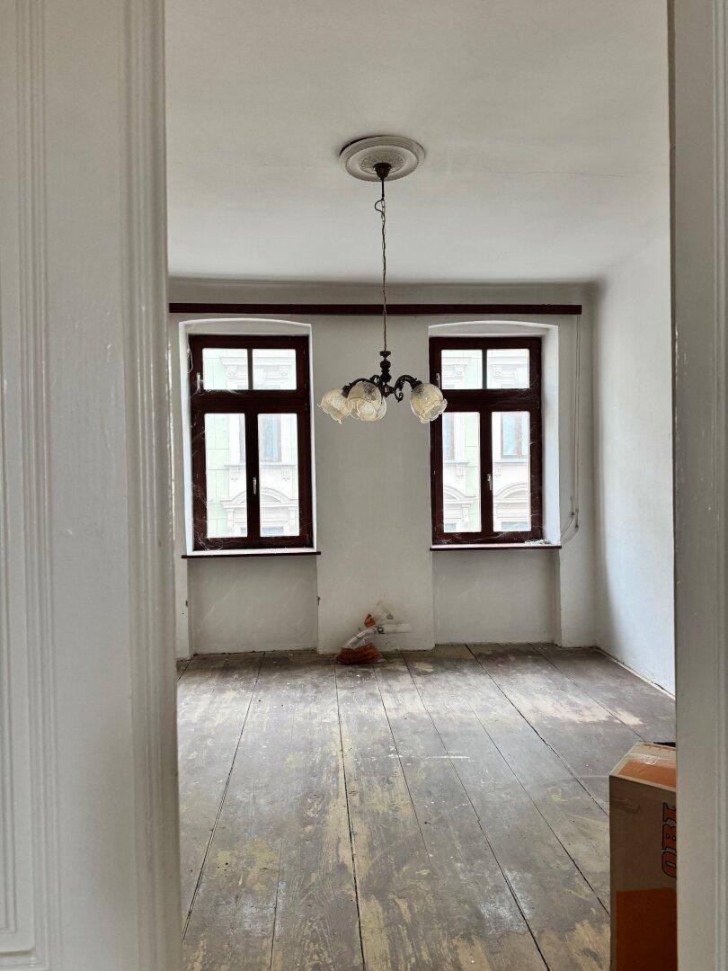 Leeres Zimmer mit Holzdielenboden und zwei hohen Fenstern, bereit zur individuellen Gestaltung.