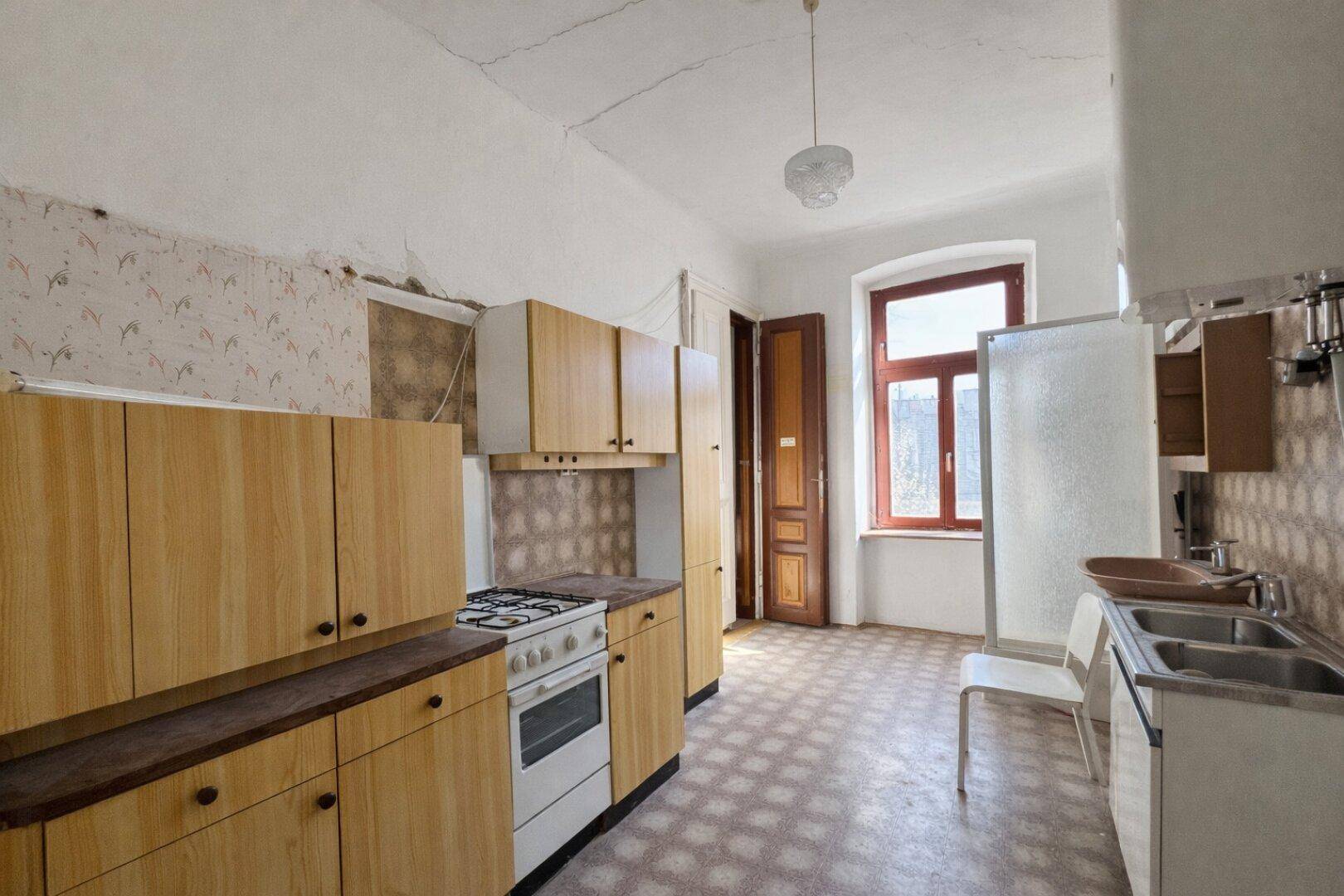 Ältere Küche mit Holzschränken, Gasherd und Spülbecken, die eine Modernisierung benötigt.