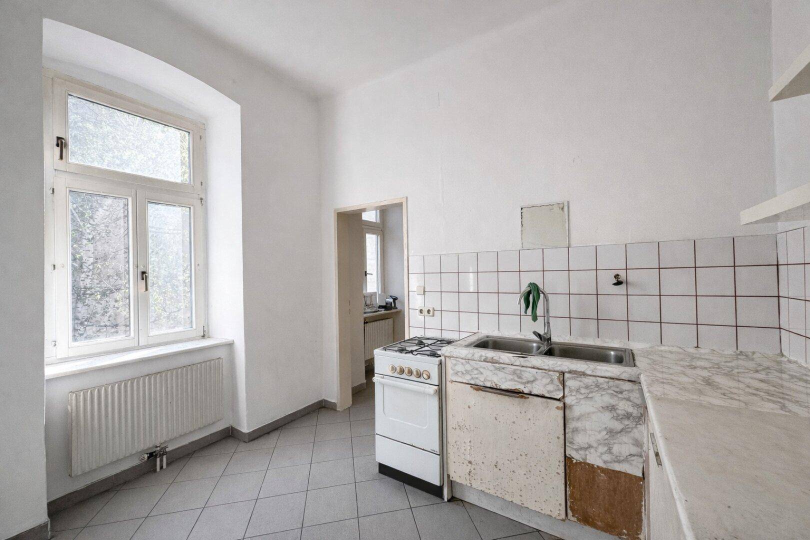 Einfache Küche mit Gasherd, Spüle und gefliesten Wänden, bereit zur Modernisierung.