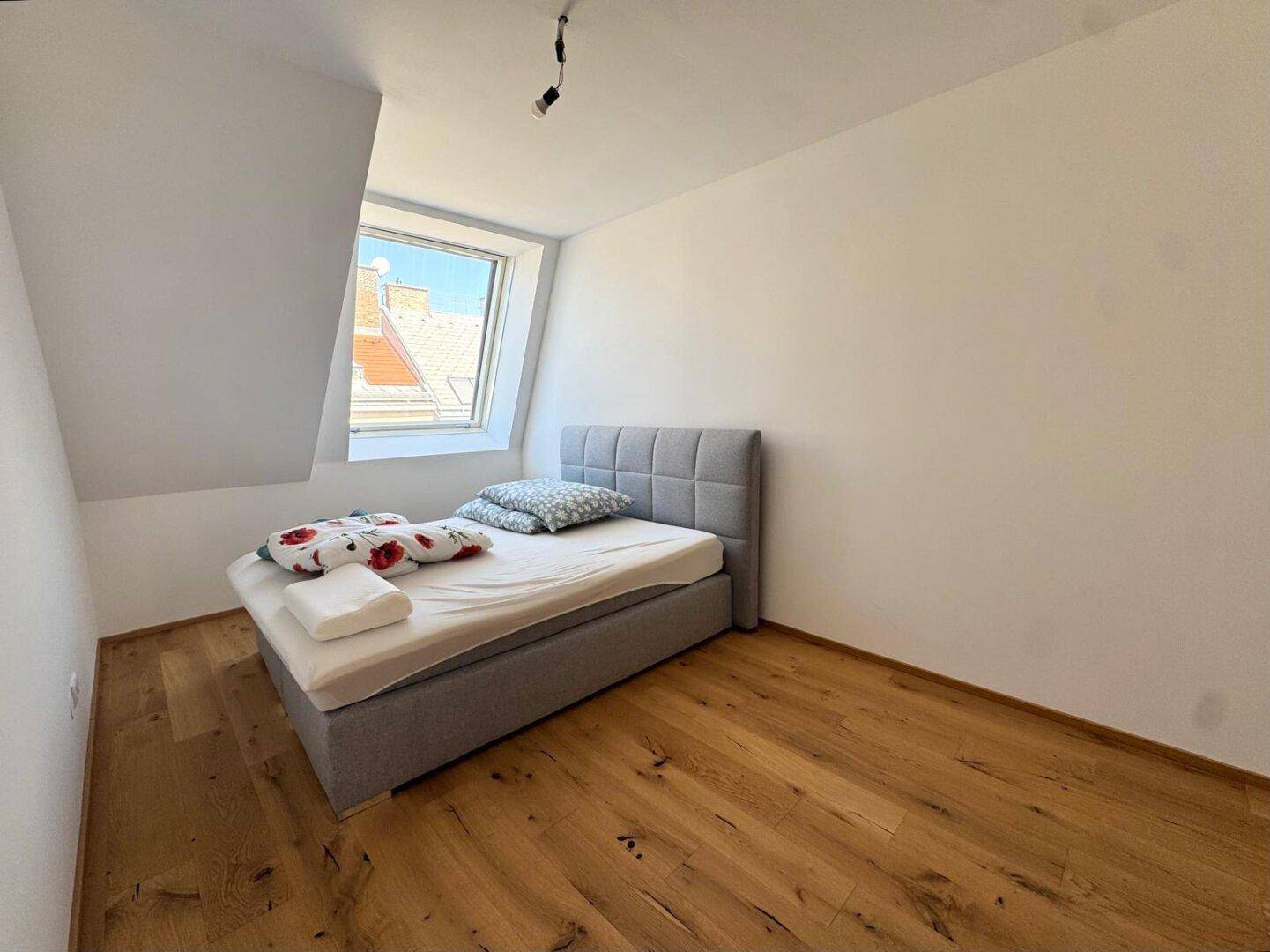 Helles Schlafzimmer im Dachgeschoss mit modernem Bett und schrägem Dachfenster.