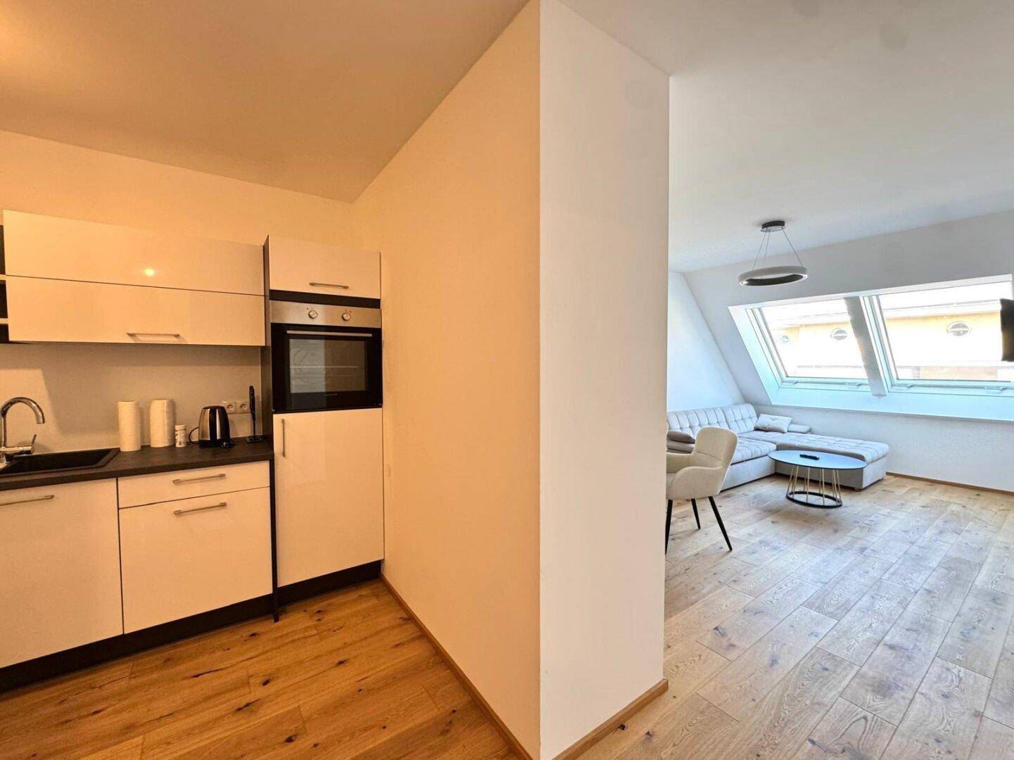 Moderne Einbauküche mit weißen Hochglanzfronten und integriertem Backofen, offen zum Wohnbereich.