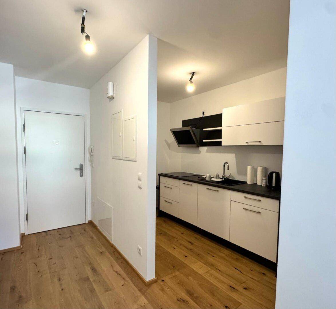 Eingangsbereich mit Holzboden und direktem Blick auf die moderne Küchenzeile.