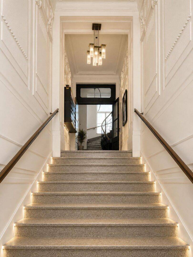 Elegantes Treppenhaus mit Stuckverzierungen, Steinboden und indirekter Beleuchtung.