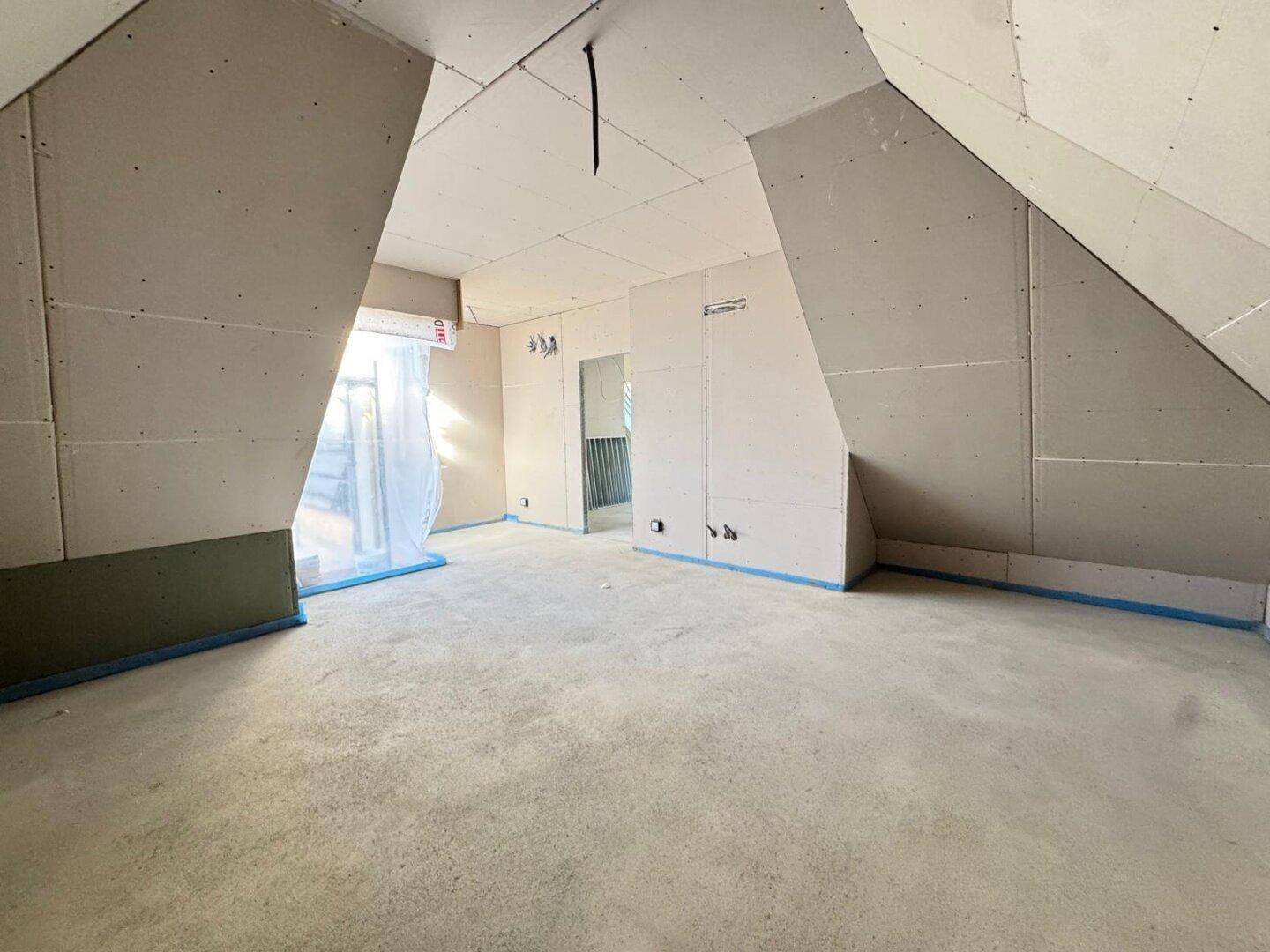 Raum im Rohbau mit Trockenbauwänden und Dachschrägen, bereit für den Innenausbau.