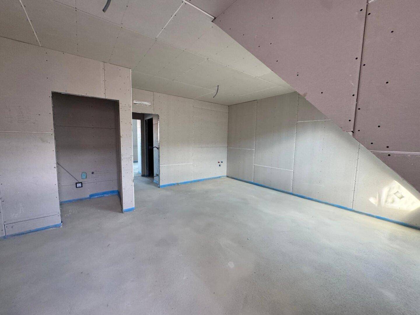 Unfertiger Raum mit Trockenbauwänden und Betonboden, bereit für den weiteren Ausbau.